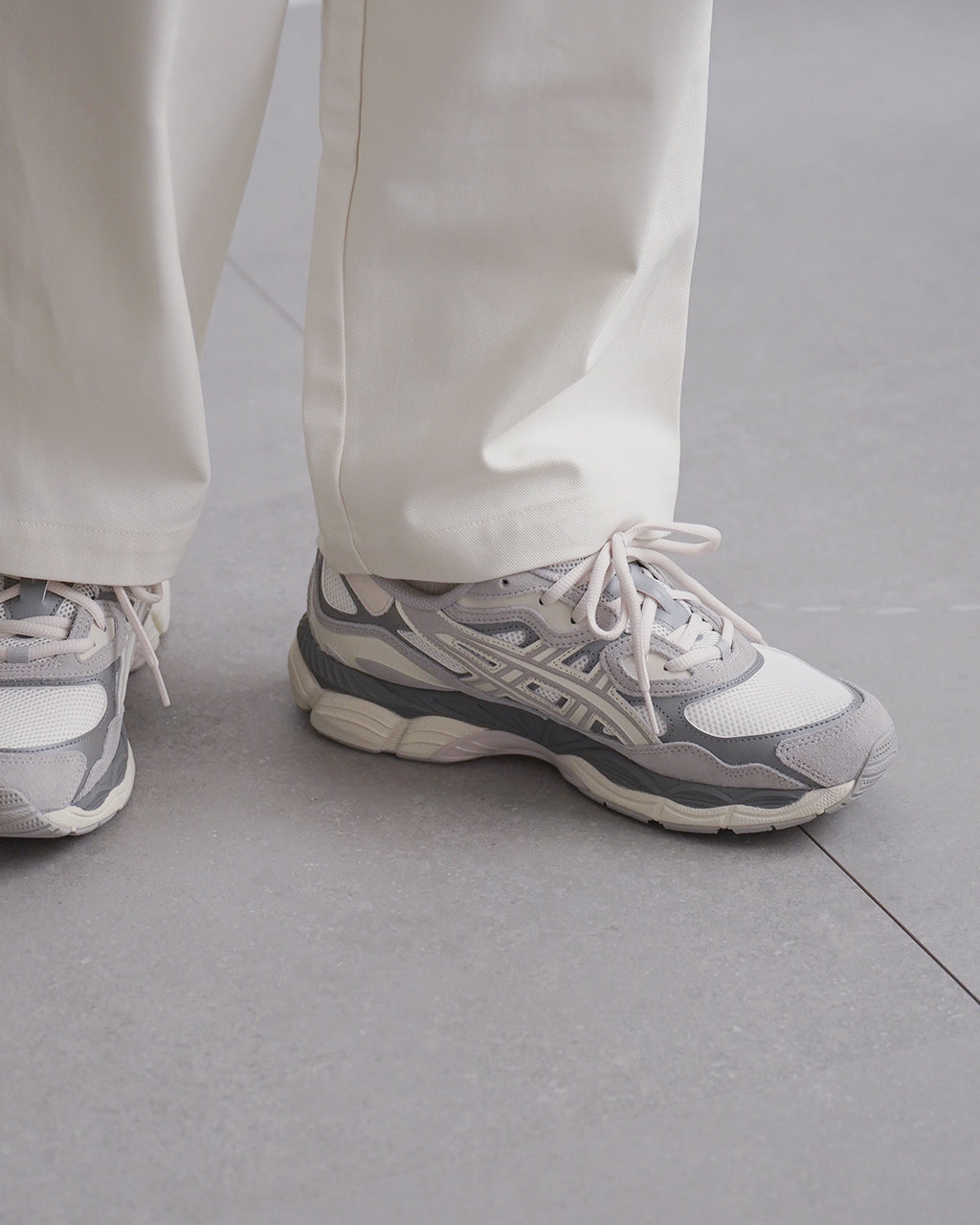 ASICS GEL-NYC 1201A789の足元アップ。白系とグレーの配色で、ソールの立体感とランニングシューズ独特の形状が見える、カジュアルなデザインのスニーカーです。