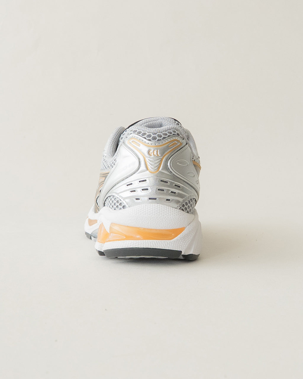 GEL-KAYANO 14の後方から撮影。銀と白を基調としたアッパーにゴールドのラインがアクセントとなるデザインで、ソールにはオレンジ色の差し色が入る様子。