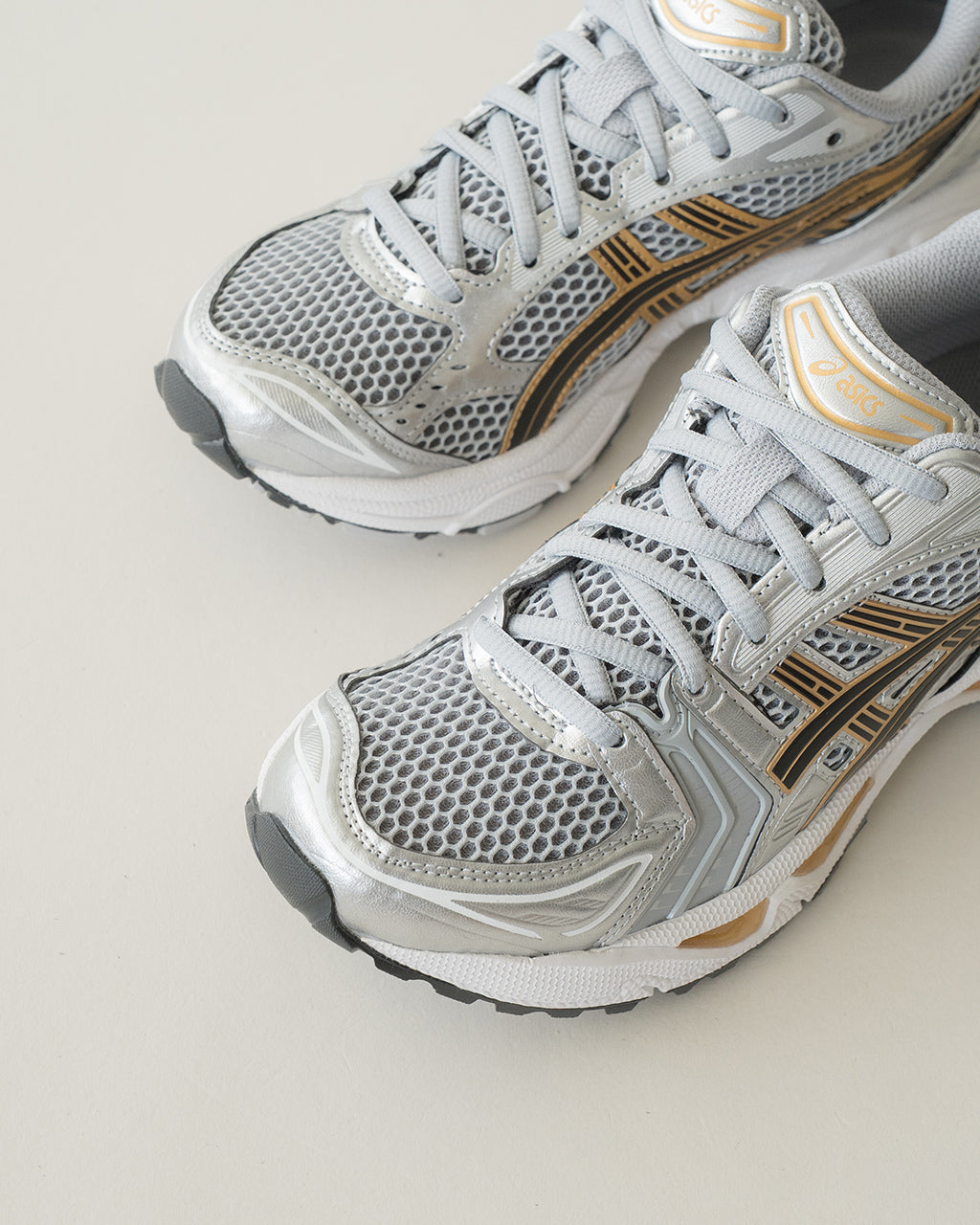 シルバーを基調としたASICS SportStyleのGEL-KAYANO 14。メッシュとオーバーレイの質感が際立つ前後左右の切り替えデザインで、ゴールドのラインがアクセントとして入っている細部写真。
