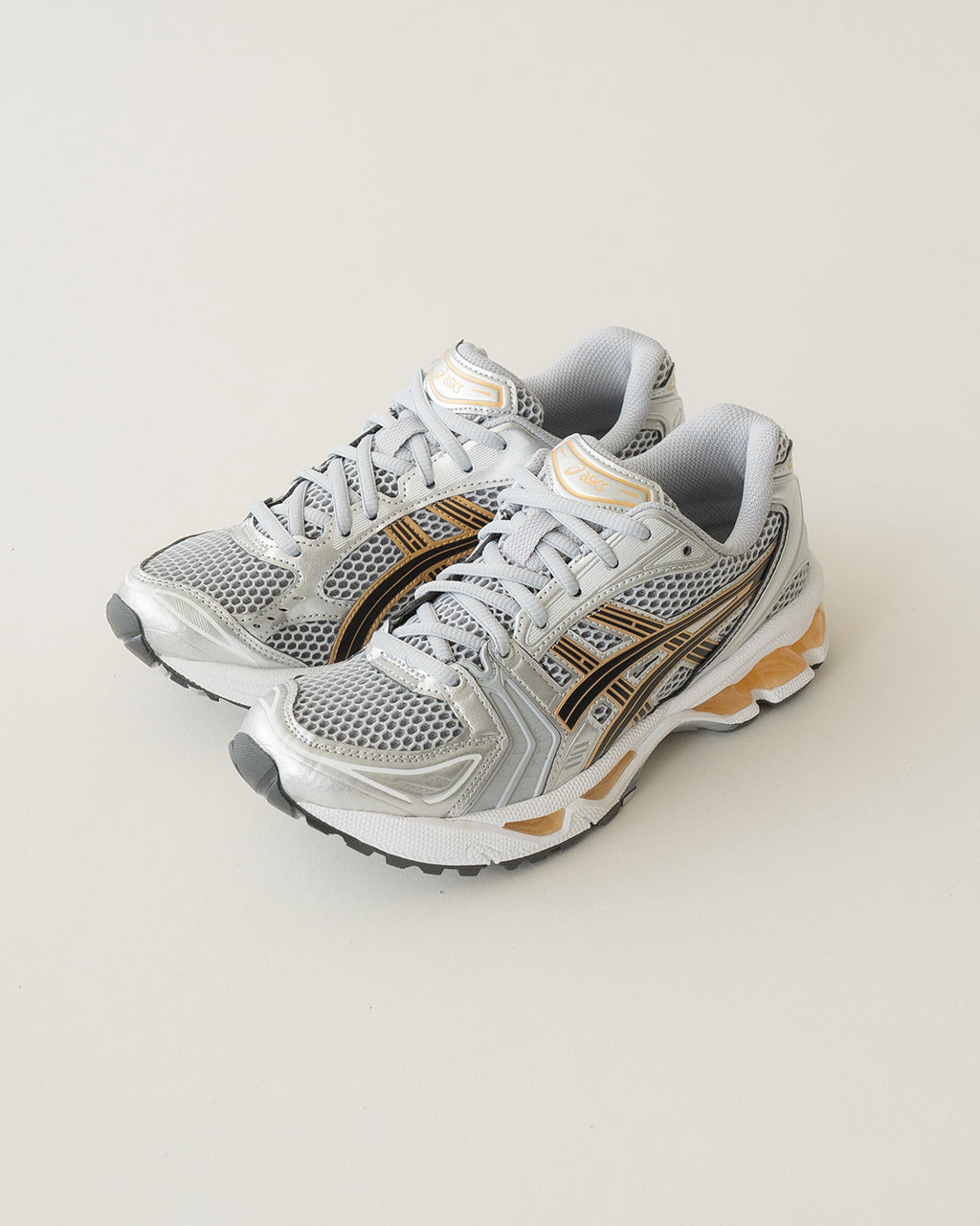 ASICSのGEL-KAYANO 14のシルバー系アッパーに黒とゴールドのラインが入ったランニングシューズ。メッシュとオーバーレイの組み合わせで立体感のあるデザインの横から見た画像。