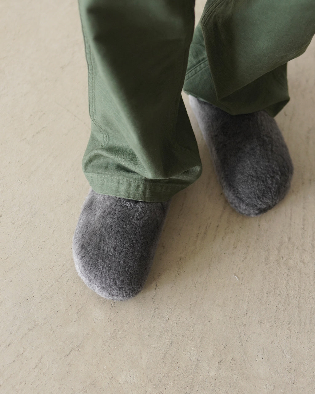 グレー系のシアリング素材と緑系パンツを着用した足元アップ。つま先まで覆う暖かな表情のサンダルが近接で見えるショット