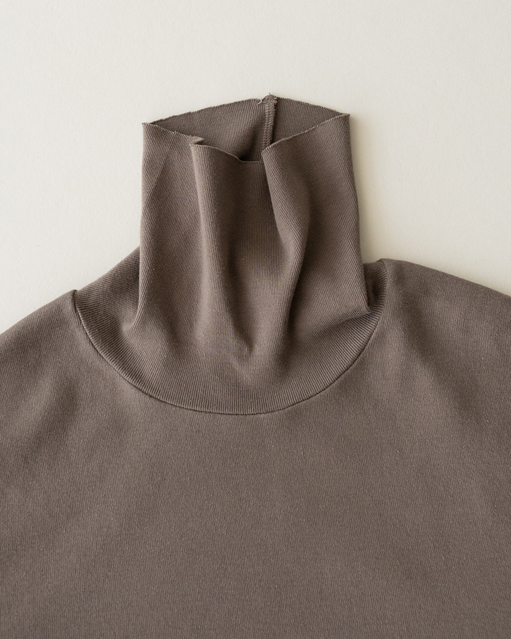 ダークグレーのタートルネック長袖Tシャツ。伸縮性のあるリブ編みで首元を包み、シンプルなデザインと微光沢の生地が落ち着いた印象。首元アップのディテールショット。