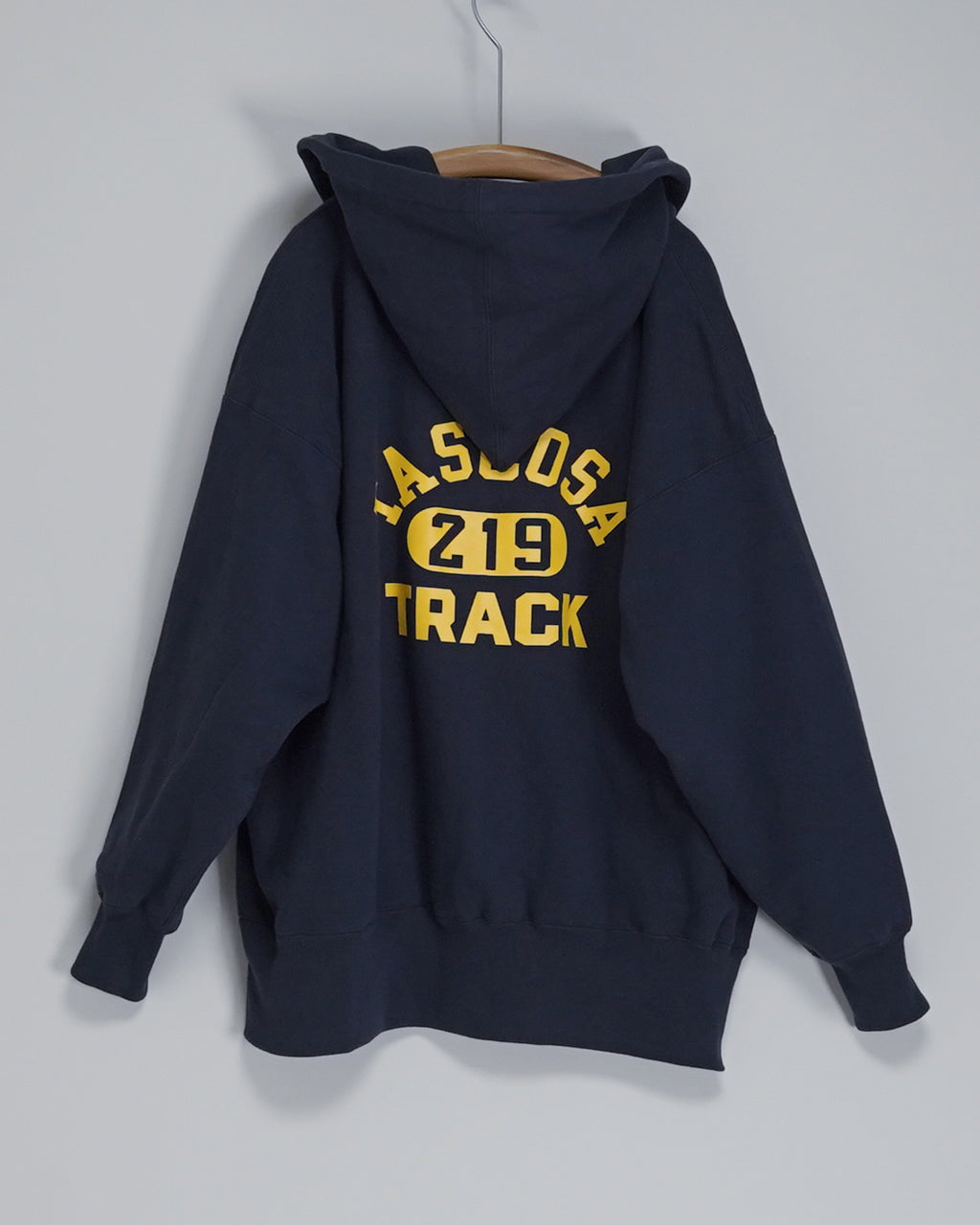 ネイビーのパーカーのバックショット。後ろ中央に黄色のプリントで「LAS LOSA  Z19 TRACK」のデザインが入る、フード付きのリラックスシルエット。袖口と裾はリブ仕様。