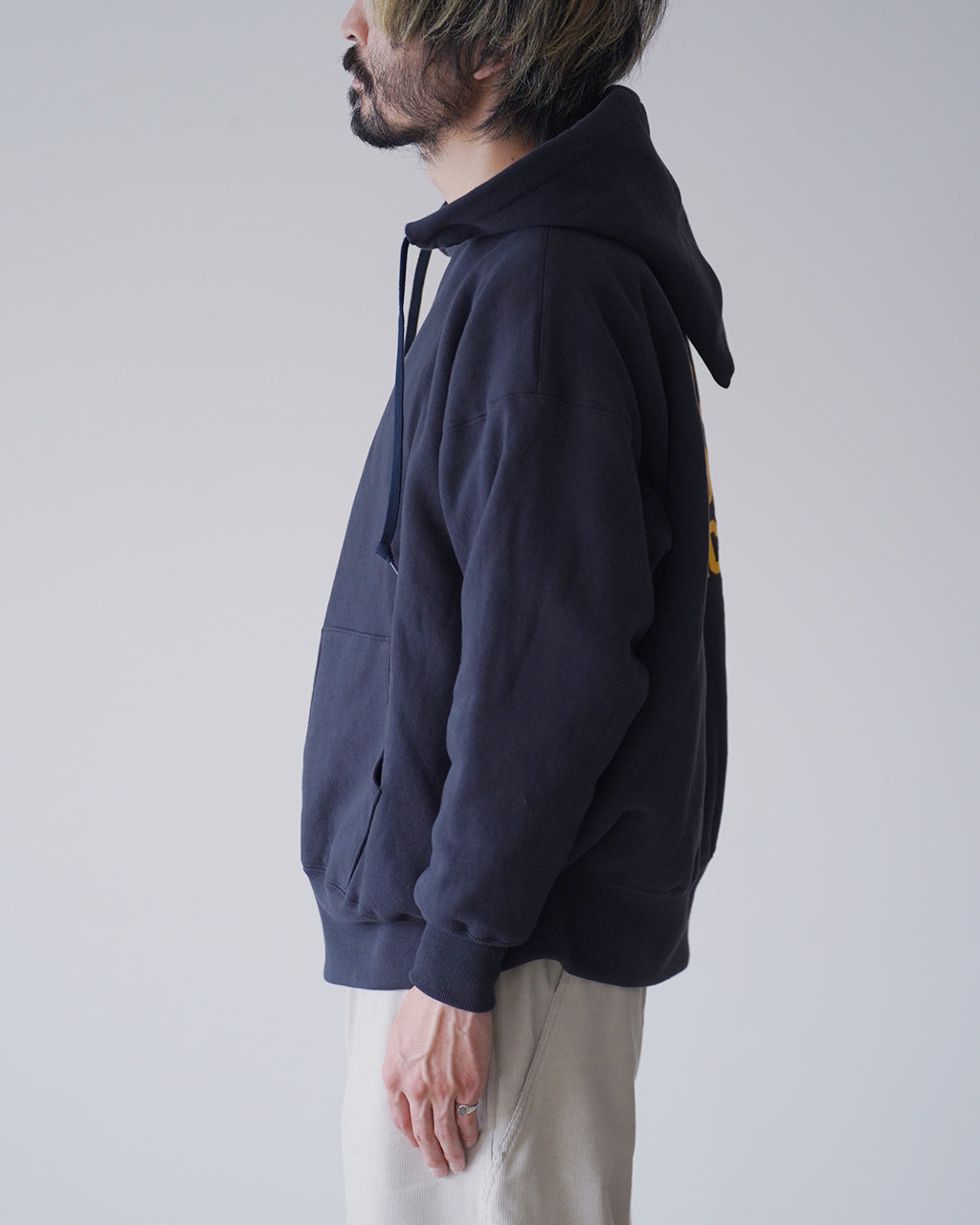 ネイビーのフード付きスウェットパーカーを横から着用した男性のシルエット。 Hoodの紐とポケット、リブ仕様が見える。