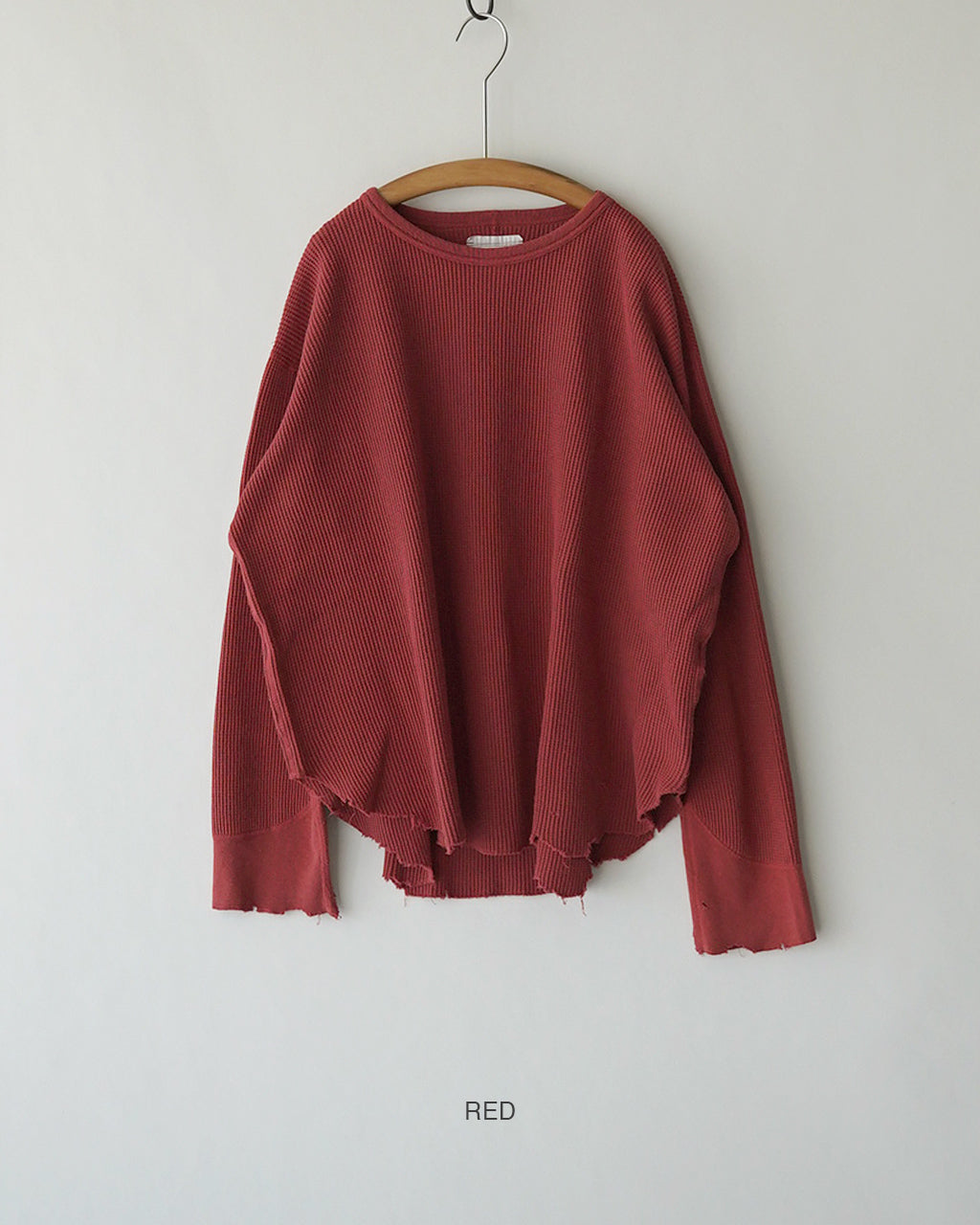 深いワインレッドのワッフル生地の長袖ニット。裾をラフに切りっぱなしにしたデザインで、前後丈の差とゆるいシルエットが特徴。