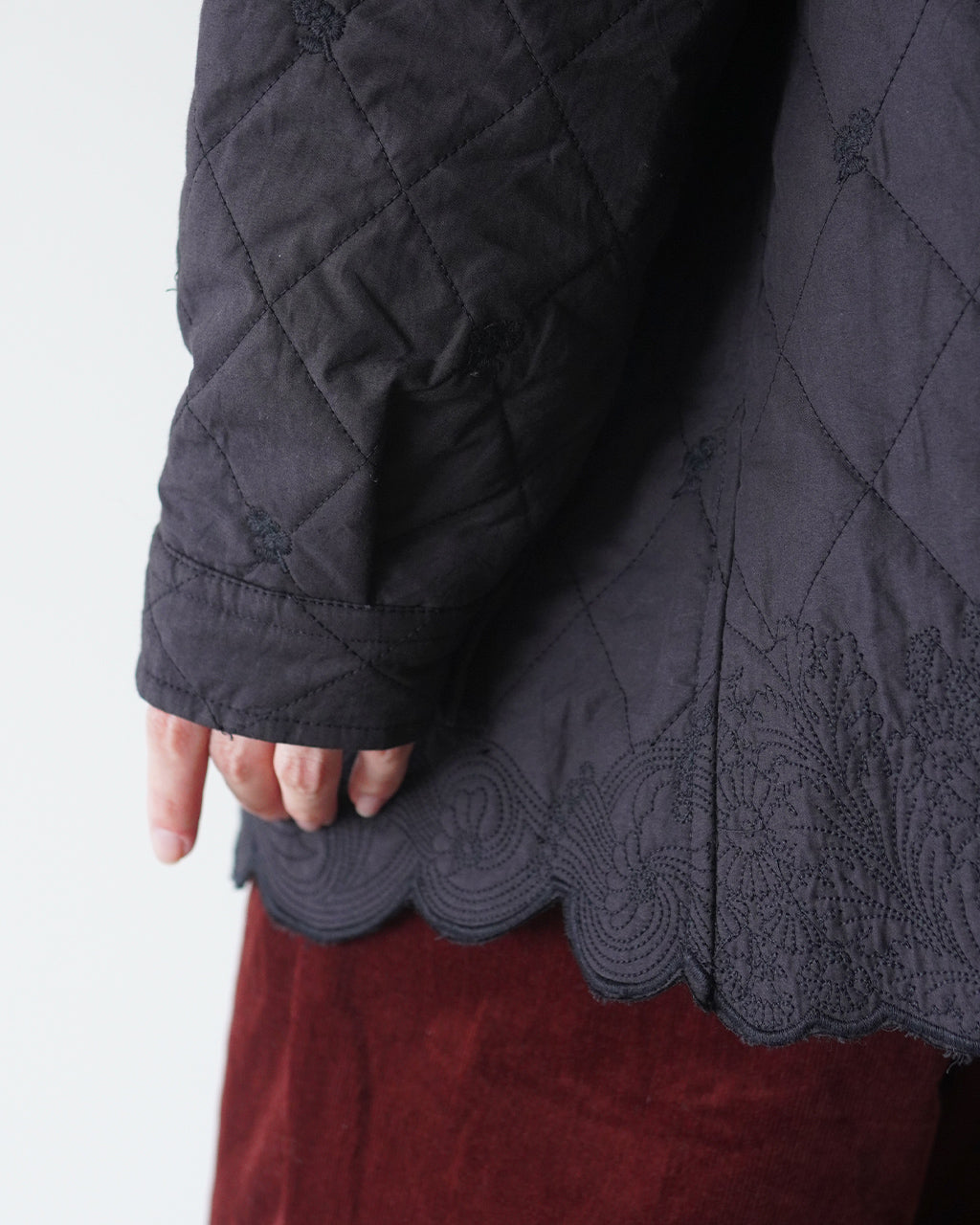 刺繍を施したスカラップの縁取りが特徴的なダークトーンのキルティングジャケット、袖口と裾の細部まで繊細な縫い目が見えるアップ写真
