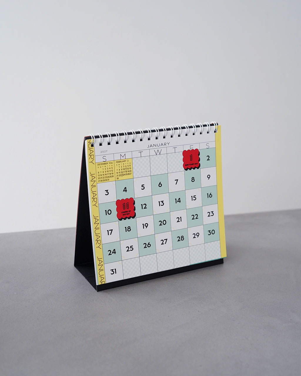幻日堂の Chess Desk CalendarCHESS-27の正面ショット。白いリング綴じと小さな卓上カレンダーがデスク上に立っている様子。カラーグリッドとカラフルなデザインが特徴的。