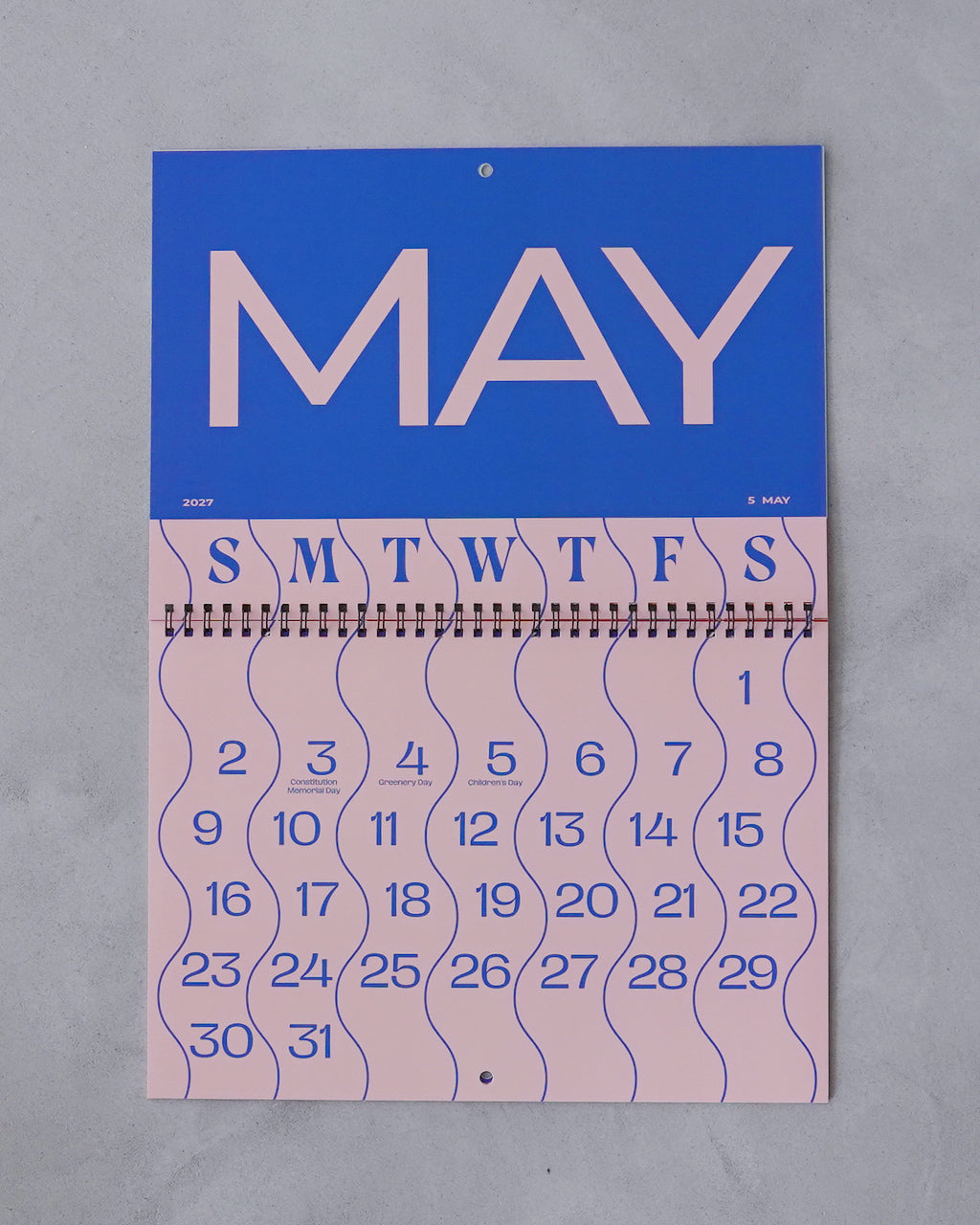 波が広がるデザインの2027年カレンダー。上部の青色背景に大きく MAY の文字、その下はピンクの月表と波形のレイアウトが特徴的なA3サイズの壁掛けカレンダー