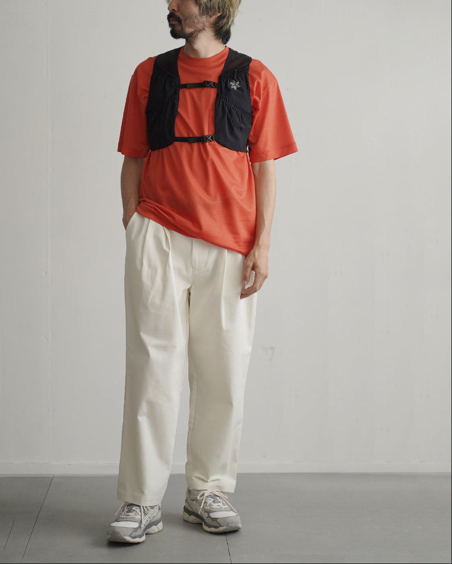赤色の半袖Tシャツに黒のベスト型ベストストラップを重ね着した男性モデルの全身写真。ベストは胸元のロゴと前後でポケット付きのデザイン。背景は淡い壁面で、動作を想定した装着イメージ。