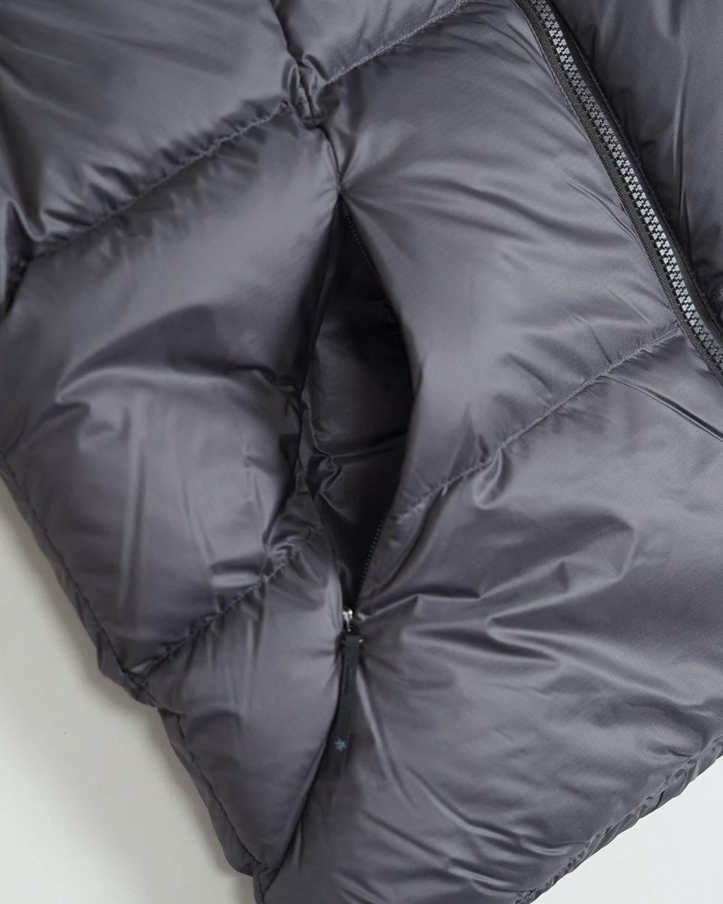ダークグレー系のダウンジャケットを zipper で開いた状態の内部ディテール。中綿の質感と縫い目のパターン、袖口付近の縫製が見える