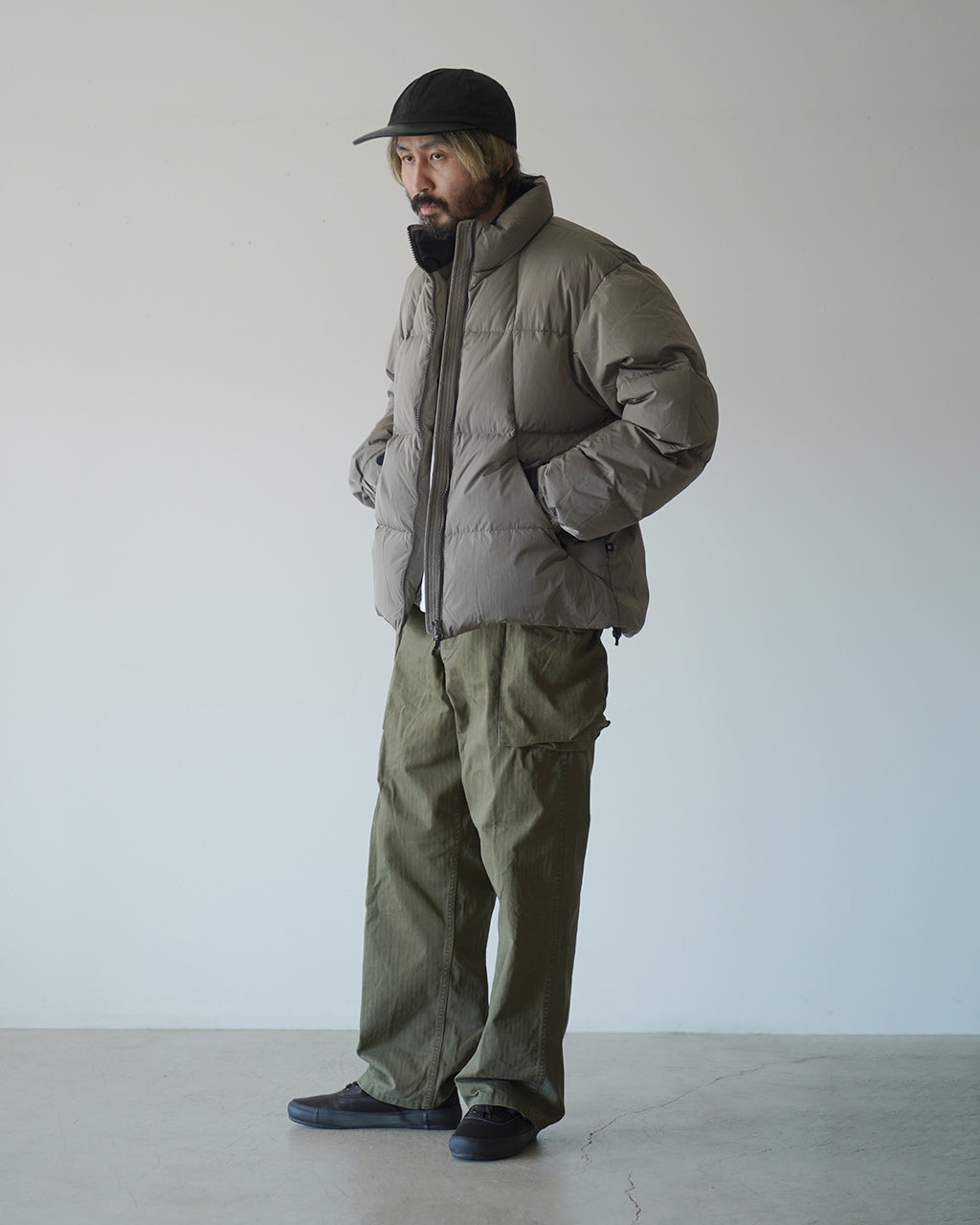 グレージュ系のDope Dyed Ripple Nylon Down Jacketを着用した男性モデル。前から見るとボリュームのあるダウンと高めの襟元、裾周りのドローコードが特徴的なジャケットの全身ショット。