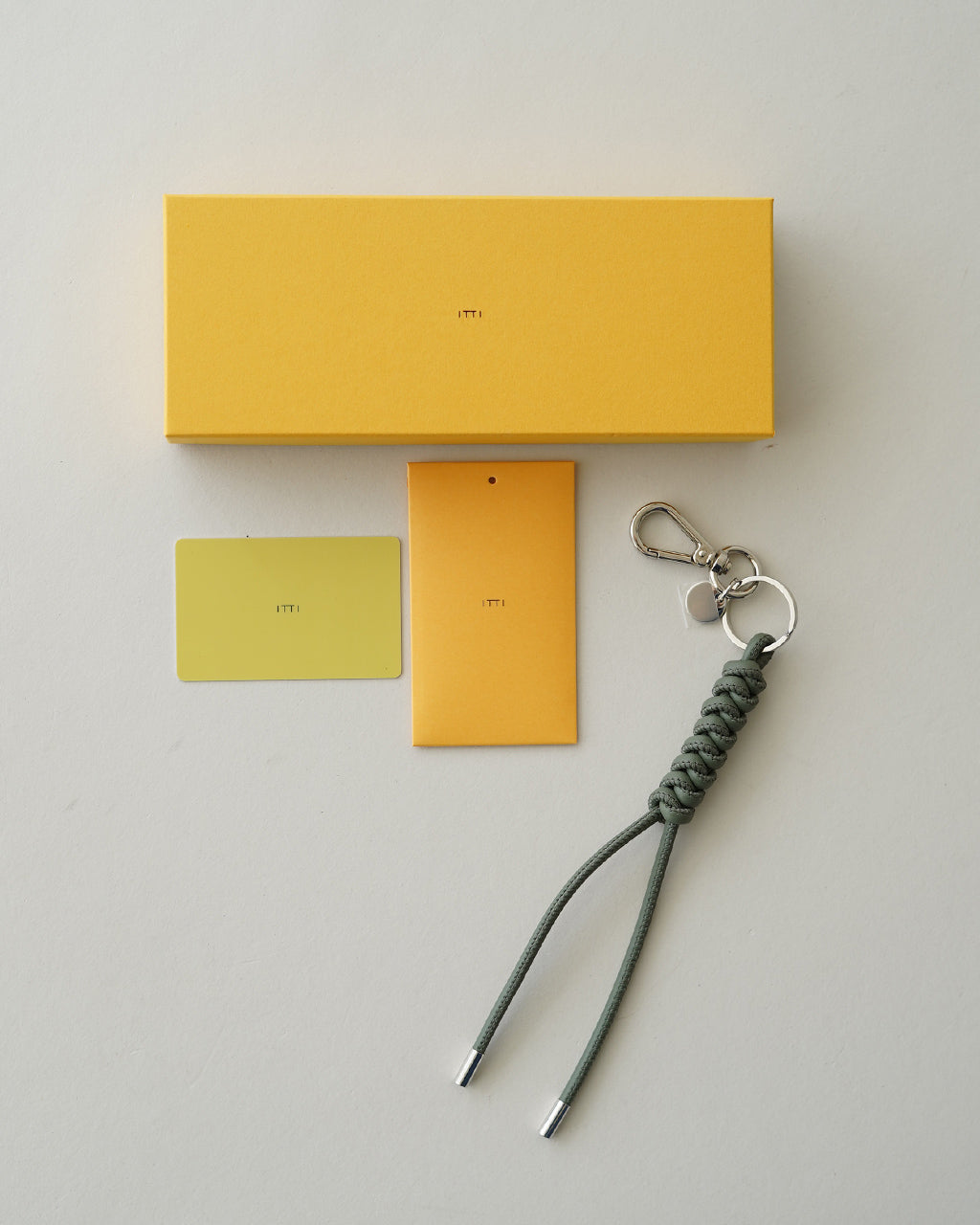 ITTIのイッチ「CRISTY SNAKEKNOT CHARM」セットのイエロー系パッケージとキーホルダー、カードとタグが並ぶ整理された部品の写真
