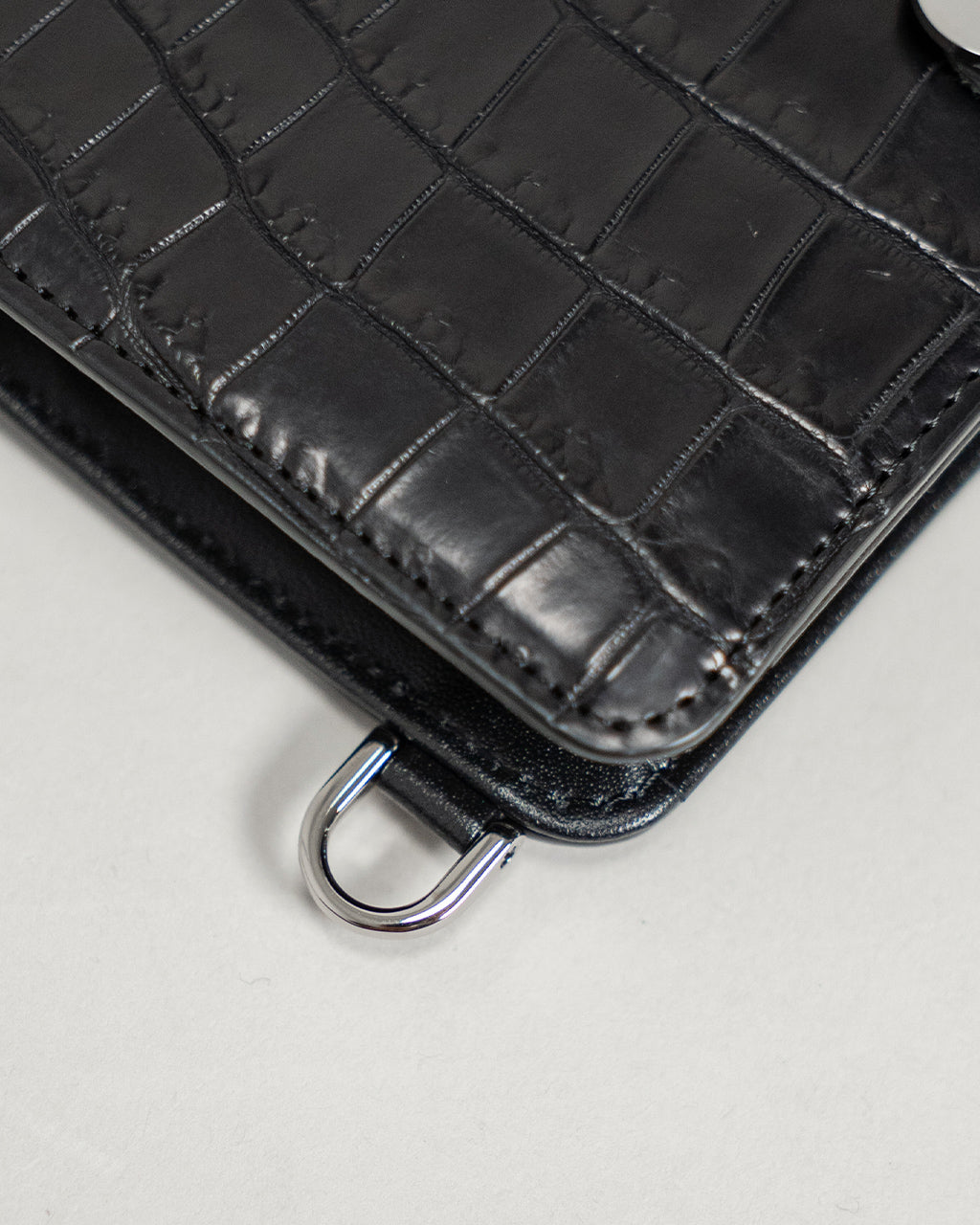 クロコダイル型押しの黒いミニウォレット。角部のステッチと光沢のある革表情が近接で分かる画像