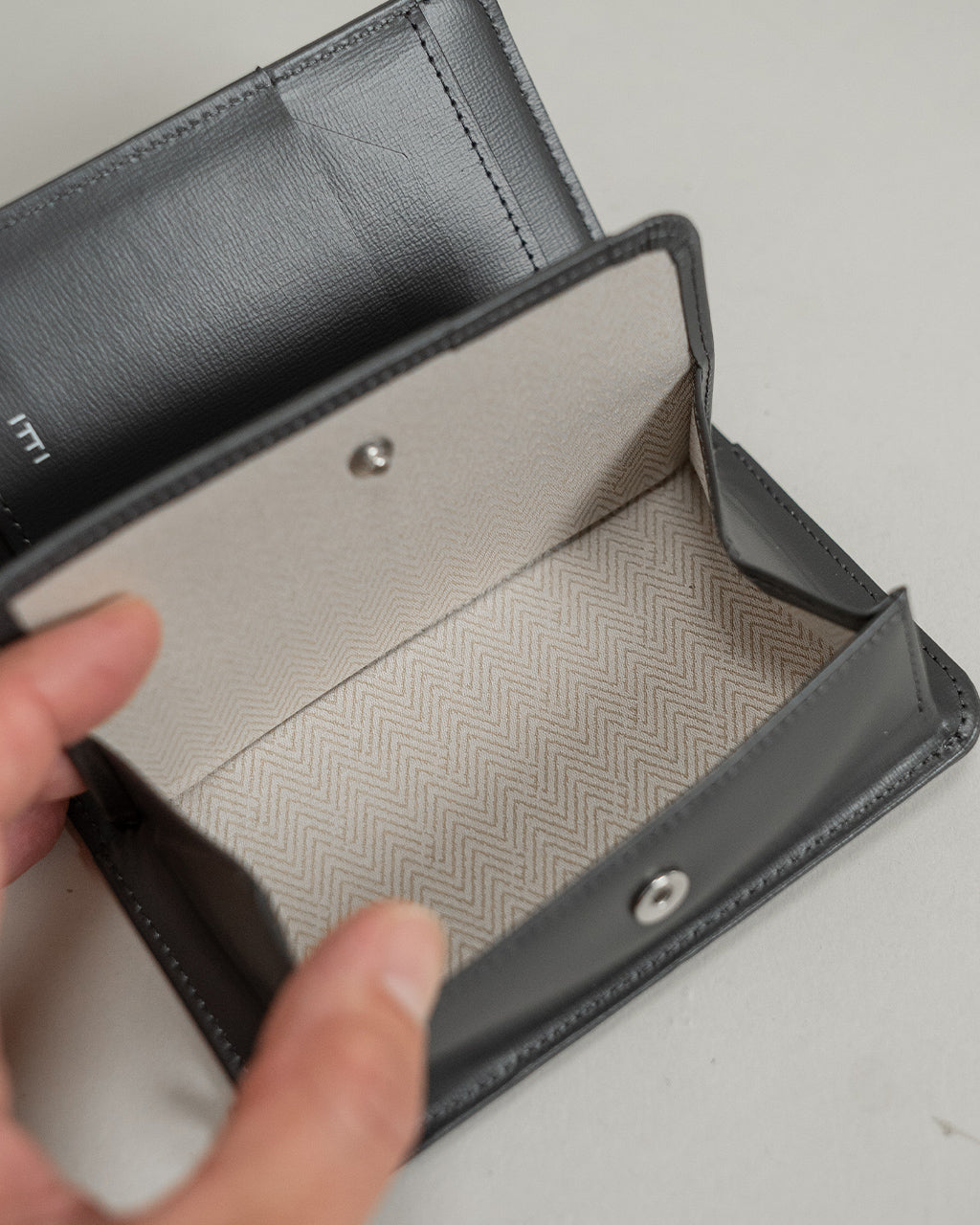 ITTIのRAPTO PREMIERシリーズの黒い財布。開閉部と内部のベージュ系生地が見え、立体的な縫製とシルバーの金具がアクセントになっている様子。