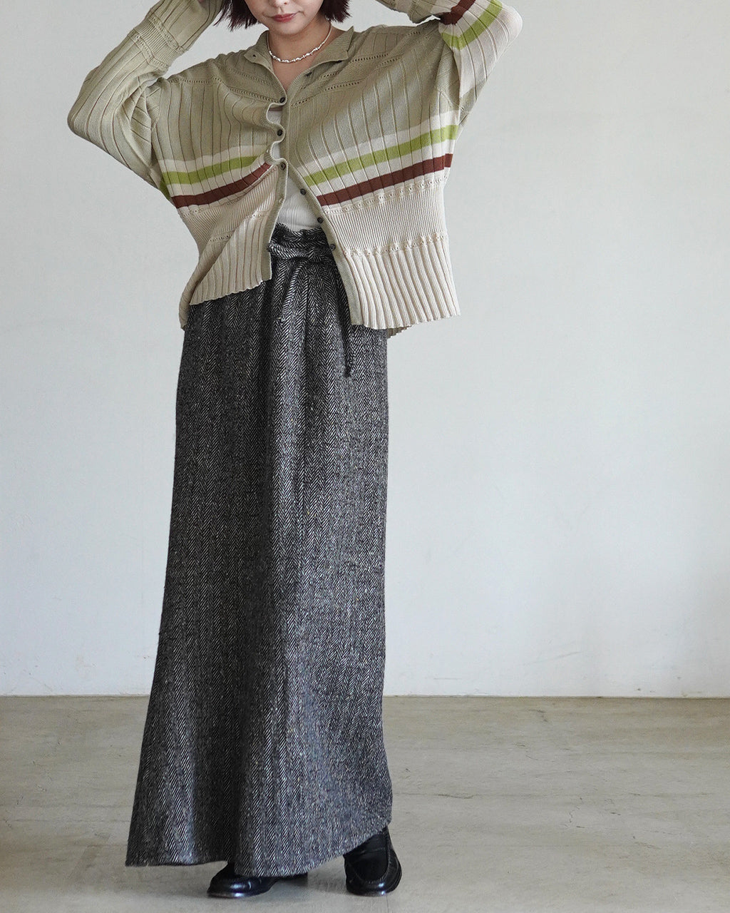ベージュ系のボーダー cardigan。前ボタンをランダムに閉じた着用イメージで、袖と裾にアイレット柄があり、軽やかな編み地とカフスのリブが特徴です。