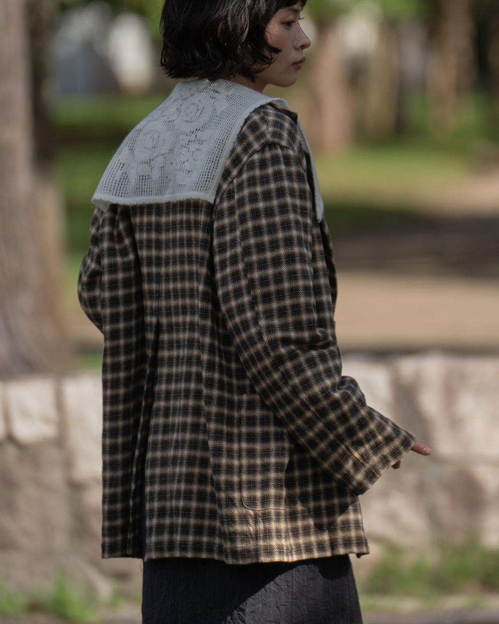 Brown-Check柄のジャケットを着用している女性の横顔と肩まわりを捉えた写真。チェック柄の生地感とゆとりのあるシルエットが見える。