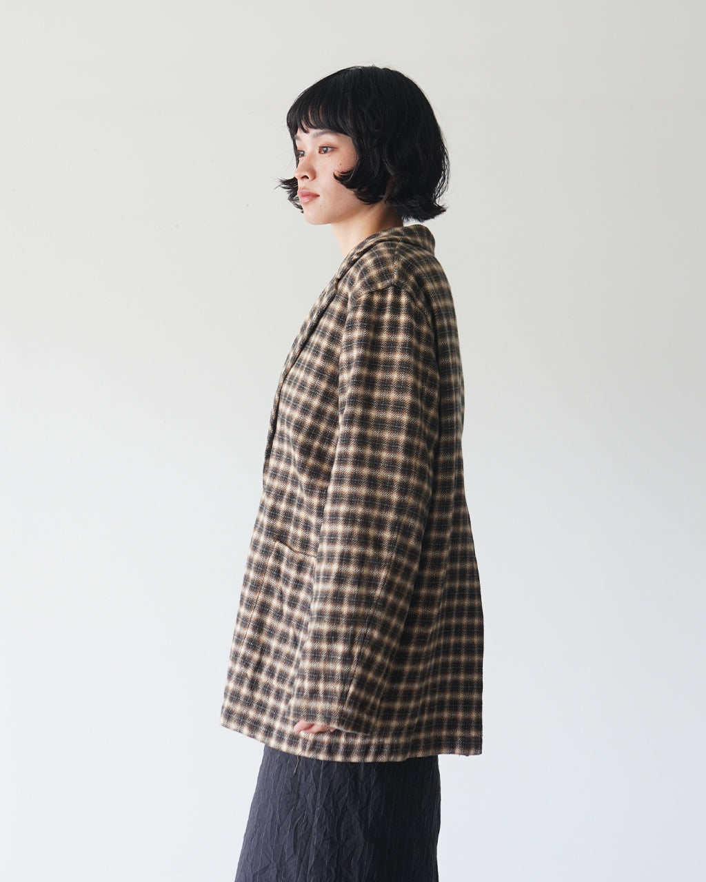 Brown-Check柄のジャケットを横から着用した女性のシルエット。ゆったりとしたシルエットと襟のラインが特徴的なデザインが分かる。