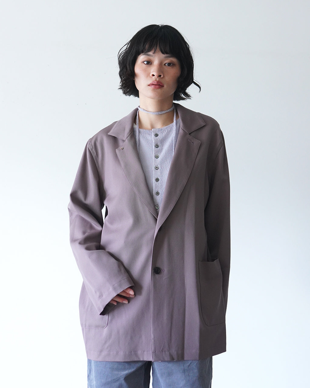 モーブのジャケットを前から着用したモデルの写真。ゆったりとしたシルエットと大きめポケットが特徴で、襟の形と袖のデザインが際立つリラックス感のある装い。