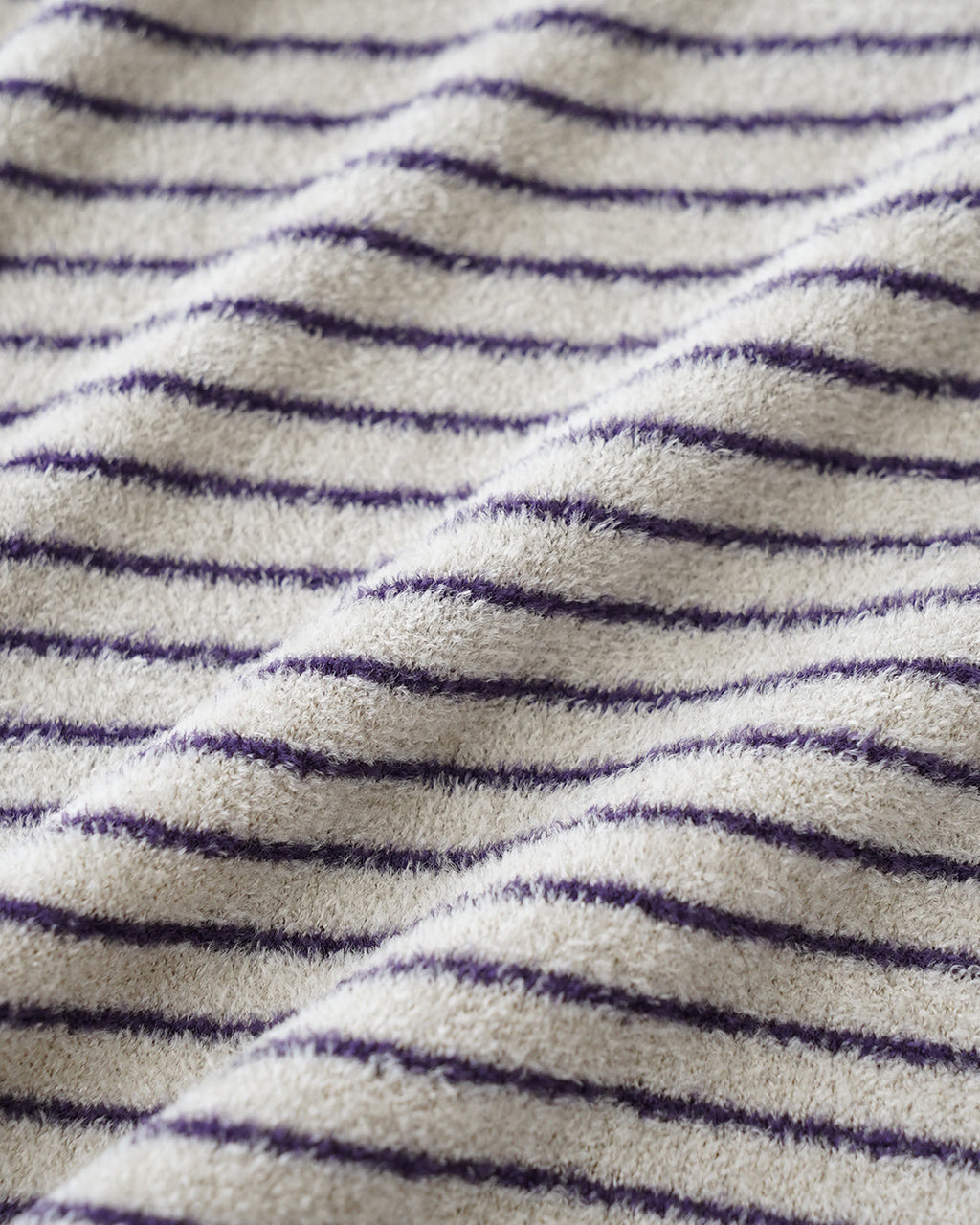 ベロア調の velour ニット生地に、淡いベージュと薄い紫色の横縞模様が入った質感のアップ画像。柔らかな起毛と光沢感が伝わる近接ショット