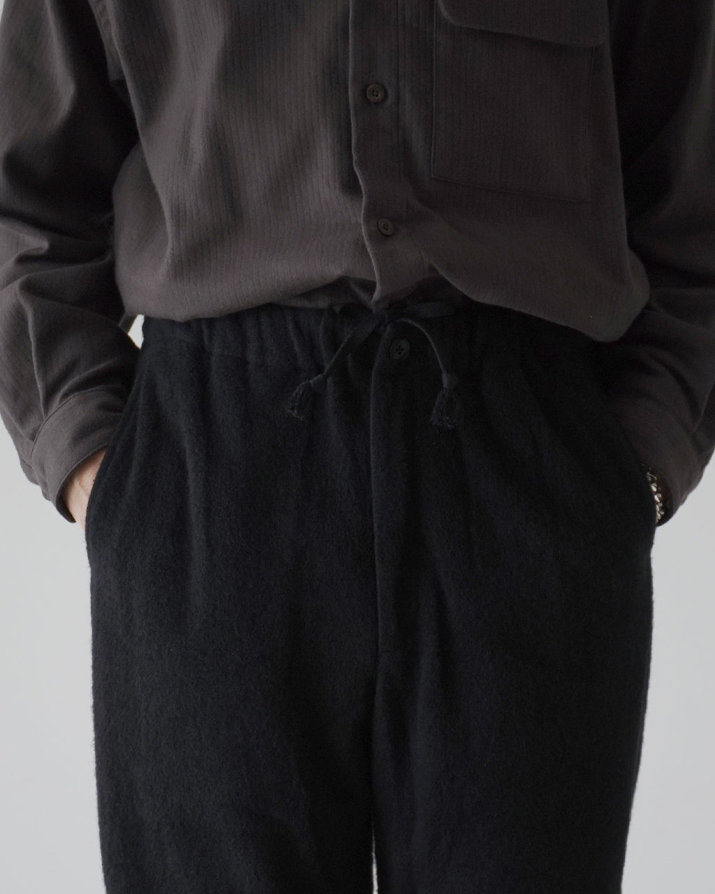 ブラックのSilk Wool Fleece Pantsの前後がわかる着用イメージ。ウエストは紐付きのリラックスシルエット、裾に向かってやや細くなるラインが見える。