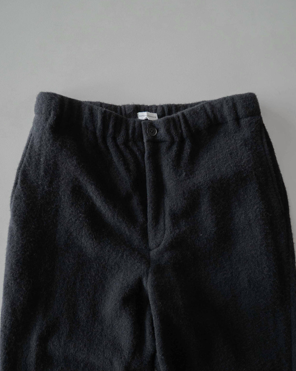 ブラックのSilk Wool Fleece Pantsのウエスト周りアップ。ゴムとドローコードのイージー仕様と前開きのディテールが見える。細かな起毛素材の質感が伝わるショット