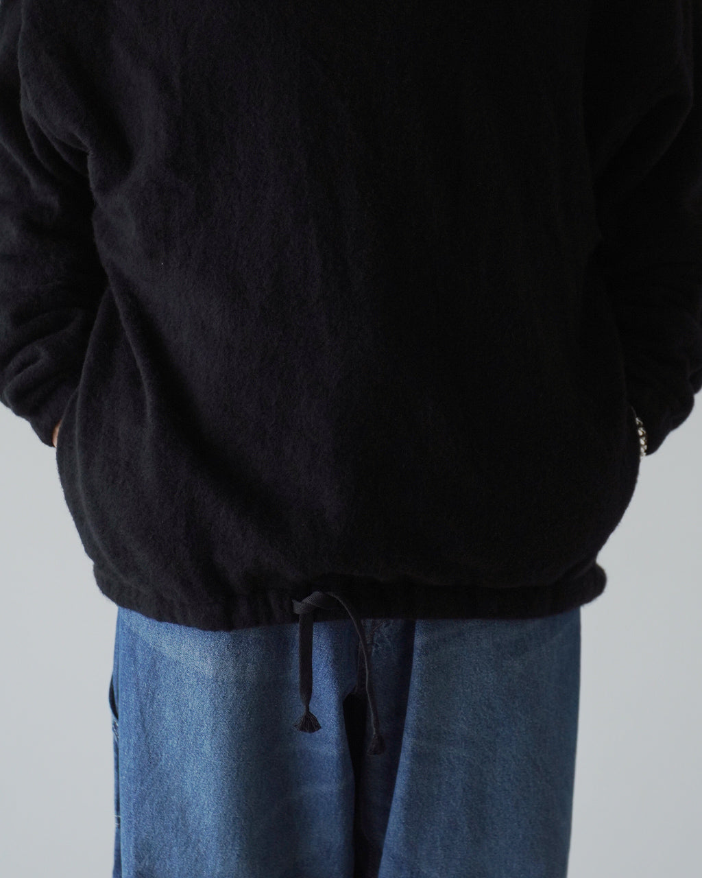 ブラックのSilk Wool Fleeceプルオーバーの背面と裾を斜め下から撮影したアングル。ウールシルクの起毛感と裾のドローコードが際立つショット