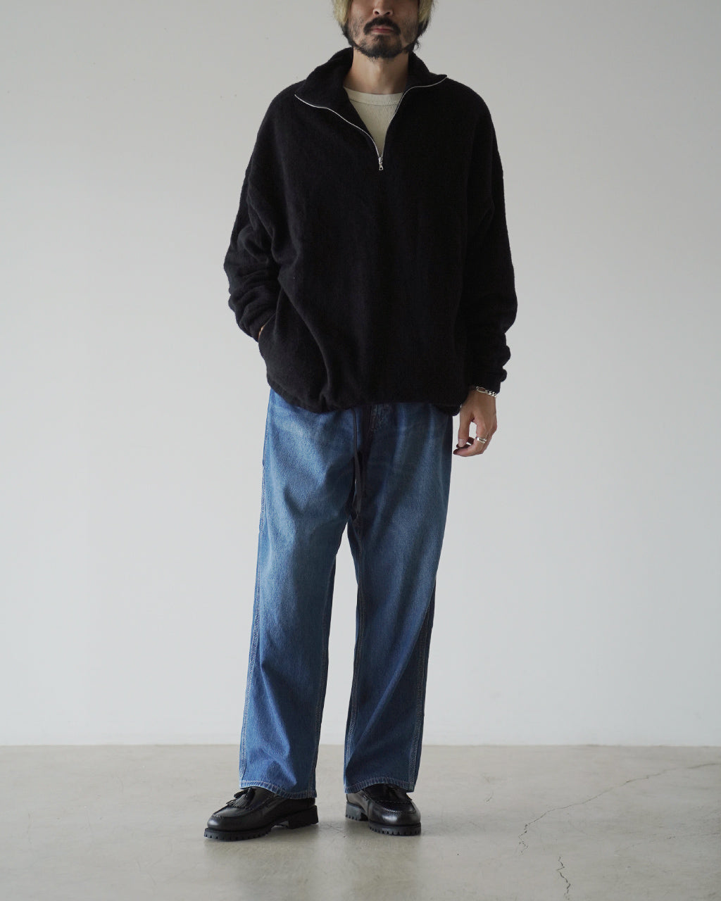 ブラックのスタンドカラー半ジップのフリースプルオーバーを着用した男性モデル。ゆったりとしたシルエットと起毛感のある質感が特徴。