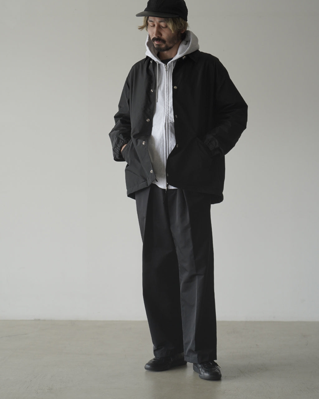 KAPTAIN SUNSHINE Unlined KS Trainer の全身写真。黒系のジャケットとパンツに、グレーのフード付きカーディガンを重ねたスタイル。