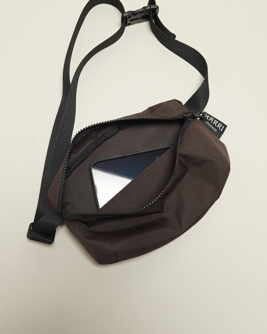 KARRI AMIACALVAのウエストバッグ。茶系の本体にジッパー付きポケットが前方に開き、スマホが収納できる収納部が見える。ショルダーストラップは黒色で長さ調整可能。