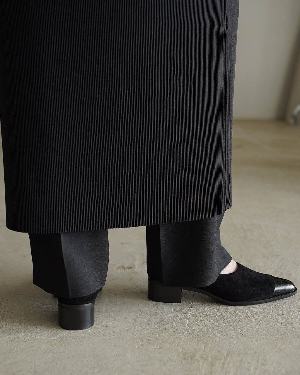 黒のパンプス、つま先が尖ったポインテッドトゥで裾からのぞくデザイン。ヒールは約4cmで安定感があり、サイドの縦スリットが特徴的なレザー素材のシンプルなシューズショット。