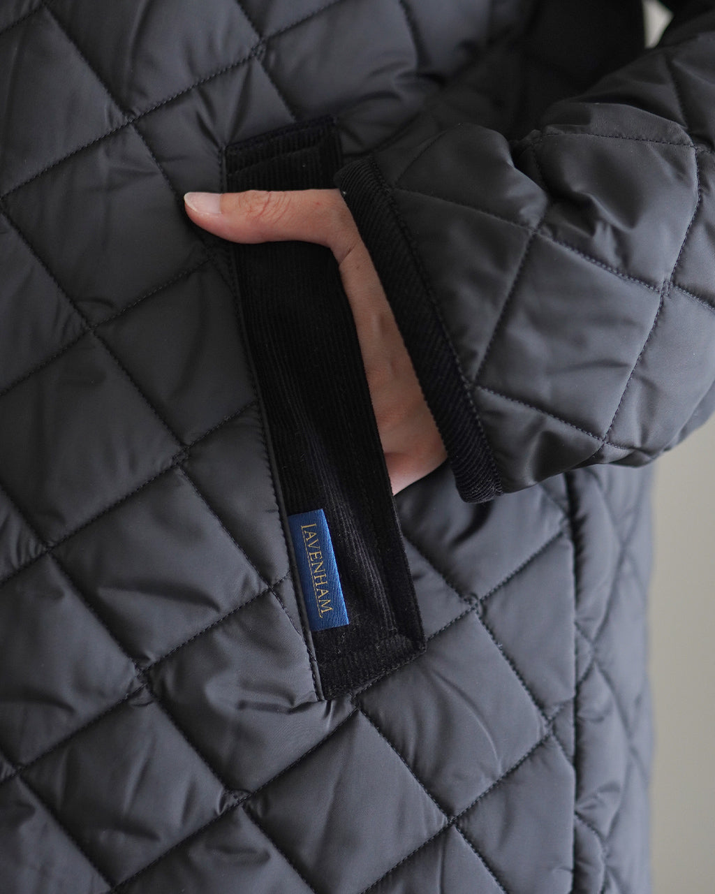 ラベンハム CHANTRY WOMENS ロングコート、ダイヤモンドキルティングのアップショット。左胸ポケット近くのストラップとブランドタグが見える。黒系の光沢ある生地感が特徴。