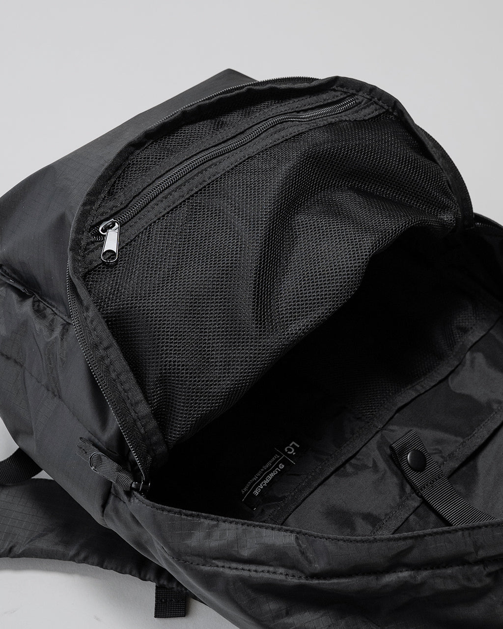 LC by LOWERCASE の DAYPACK LITE 20Lの開閉部アップ。前室ファスナーと内側メッシュポケットが見える黒いリュックの内装写真