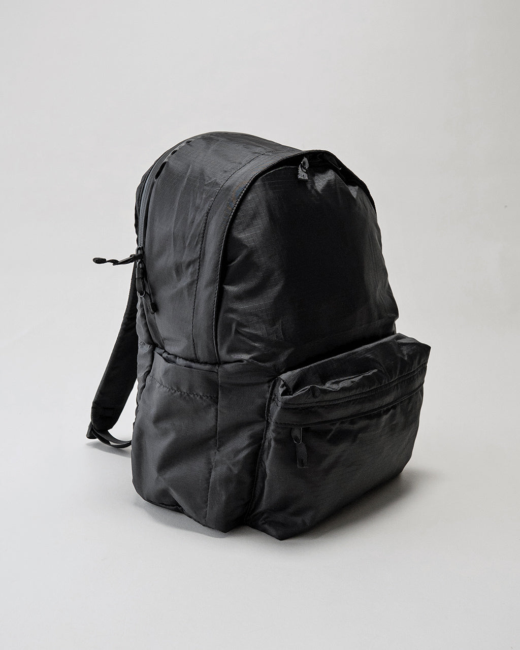 LC by LOWERCASEの DAYPACK LITE 20L、黒系のシンプルなデザイン。前方から見える大容量フロントポケットと側面ポケット、背面にはパッドのないリュック本体の総柄ニュアンスが特徴的