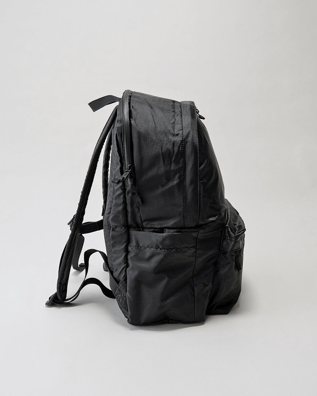 LC by LOWERCASEの DAYPACK LITE 20L。黒系のバックパックを横から見たシルエット、側面ポケットと背面ジップのディテールが確認できる写真。
