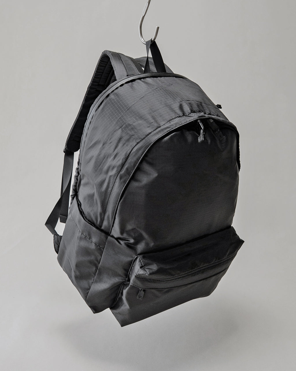 LC DAYPACK LITE 30Lの正面からの画像。黒系の軽量ナイロン生地で、前面ジップポケットとメイン開口部のファスナーが見える。背面側のショルダーパッドがやや見える構図。
