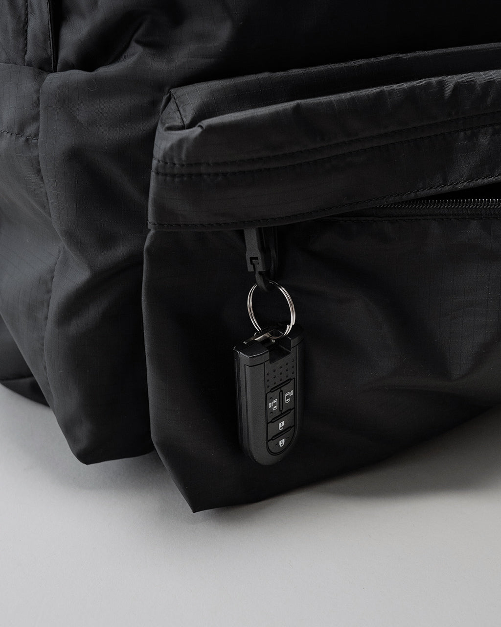 LC by LOWERCASEの DAYPACK LITE 30Lの黒色ファスナー付きポケット横から見えるジップと鍵ホルダーが特徴的なディテールショット