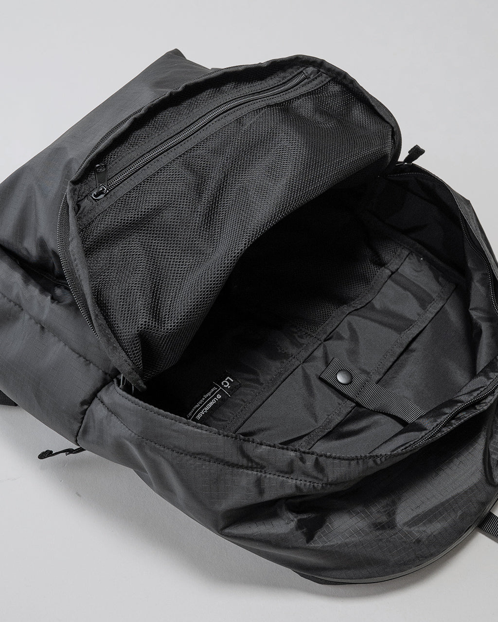 LC by LOWERCASE の DAYPACK LITE 30L。黒系のリュックで、内部には仕切りポケットとメッシュポケットが見える。開閉は前面ジップ付きポケットが特徴的。