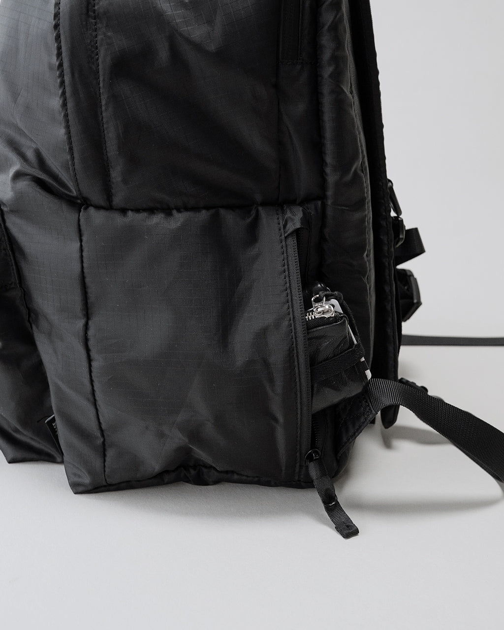 黒系カラーのLC Daypack Lite 30Lの側面と下部ファスナー周りが写るダークトーンのディテールショット。素材感の微細なテクスチャと縫製のラインが確認できる。