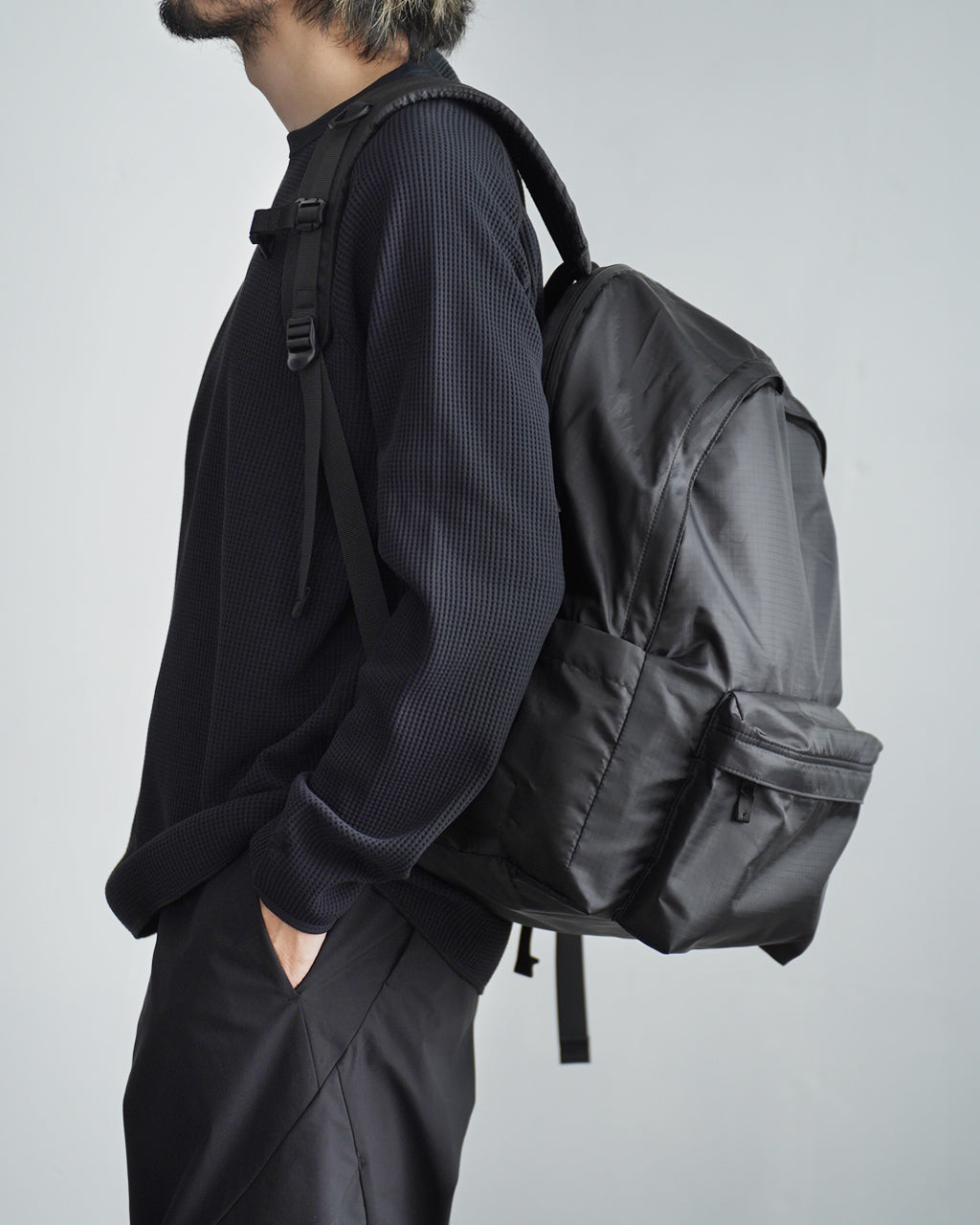 LC by LOWERCASE の DAYPACK LITE 30Lを背負い、黒系の軽量バックパックと着用者の横姿を写した画像。シンプルなデザインと丈夫なナイロン素材感が伝わる