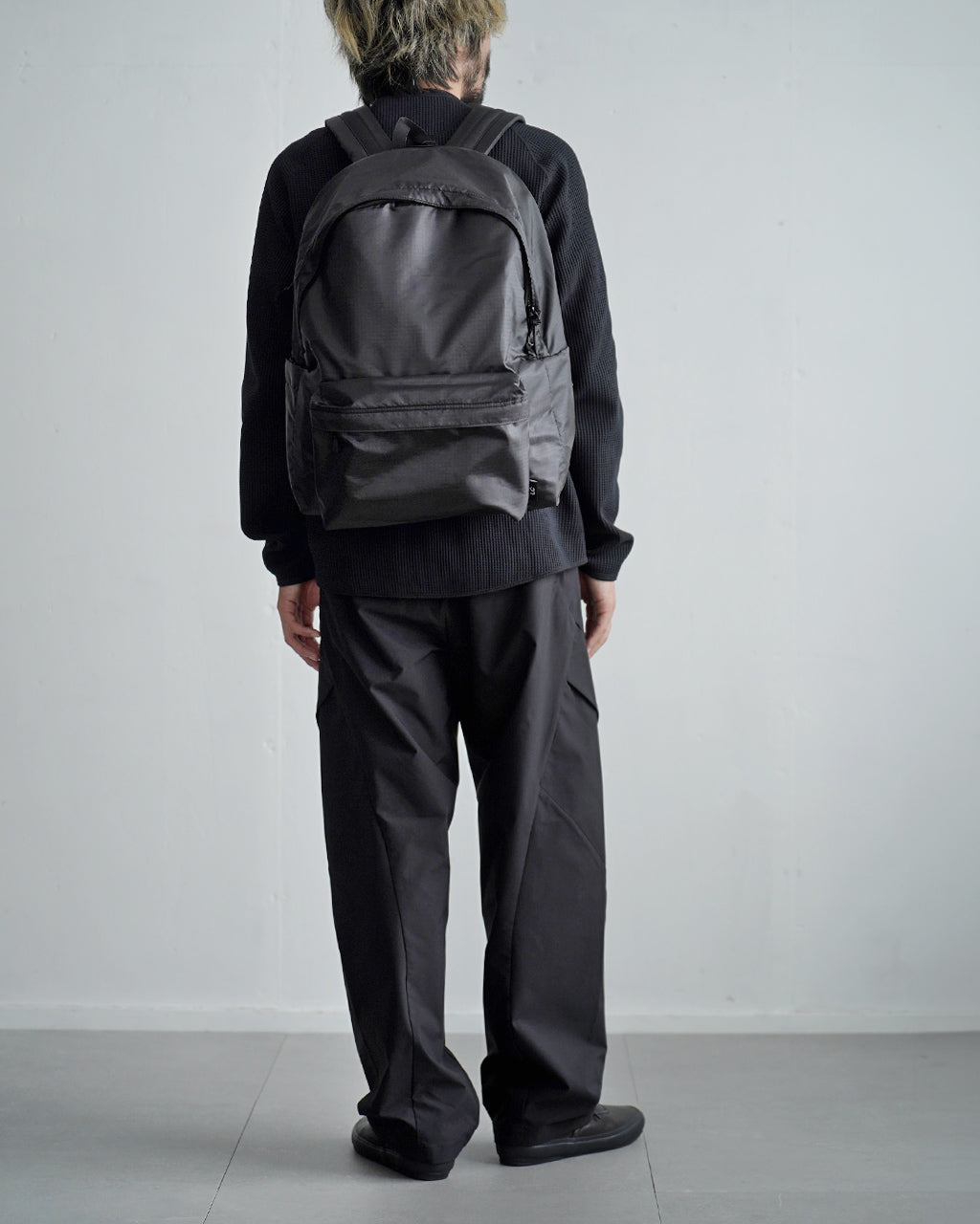 LC by LOWERCASE の DAYPACK LITE 30Lを背負い、前後は黒系のシンプルなデザイン。大容量のメイン収納と前部ポケットの形が見える背面ショット