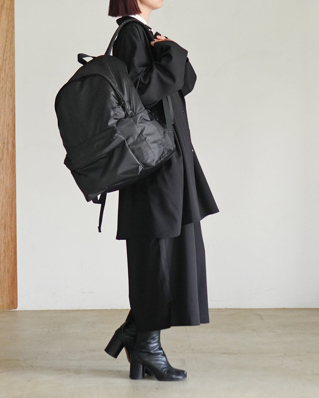 黒のLC by LOWERCASE LC DAYPACK LITE 30Lを肩に掛けた女性の横姿。軽量なリュックを背負い、全体はモードなブラック系で統一されている。