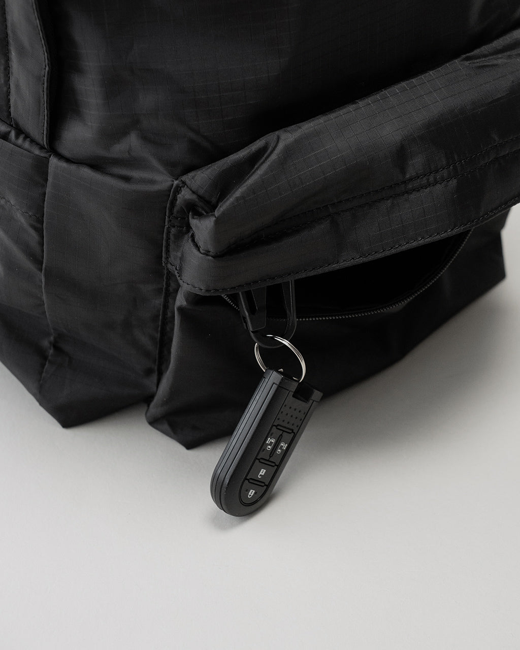 LC by LOWERCASE の DAYPACK LITE 16L の黒色外観。ジッパー付きポケットとキーホルダーが付いた角部のディテールが見える。軽量ナイロン生地の質感が近接で確認できる画像。