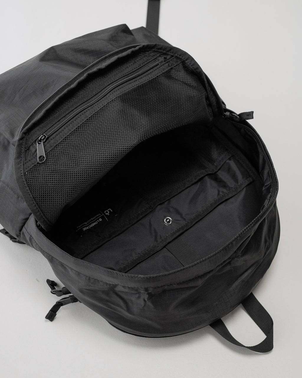 LC by LOWERCASEの DAYPACK LITE 16L ブラック系のバックパック。開口部は大きなジッパーで中はメッシュポケットと内ポケットが見える。シンプルな外観と軽量素材が特徴のリュックサック。