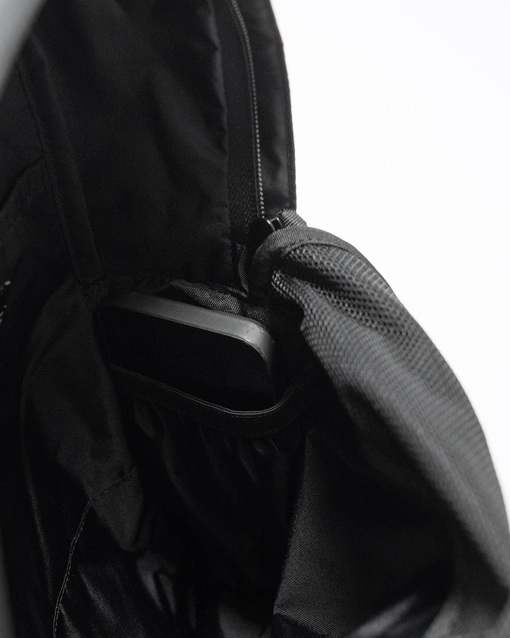 LC by LOWERCASE の DAYPACK LITE 16L の内部ポケットとスマホなどを収納できる小さめのポケットが見える、ブラックのバックパック前面とサイド端部のディテール写真