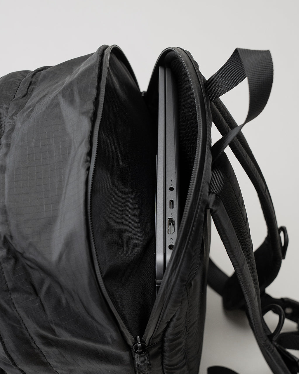 LC by LOWERCASEのDAYPACK LITE 16Lの側面とジッパー部が見えるブラックのバックパック。薄手の素材感と細いストラップが特徴的。