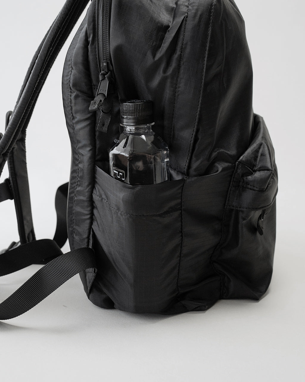 LC by LOWERCASEの DAYPACK LITE 16Lのサイドポケットに水筒が入った、ブラック系のバックパック背面とサイドカバーの近接ショット