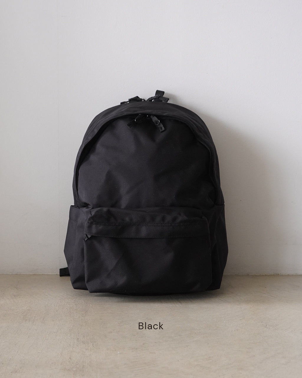 ブラックの DAYPACK Msize の正面全体像。シンプルで丸みのあるフォルムと前面ポケットが目立つ。