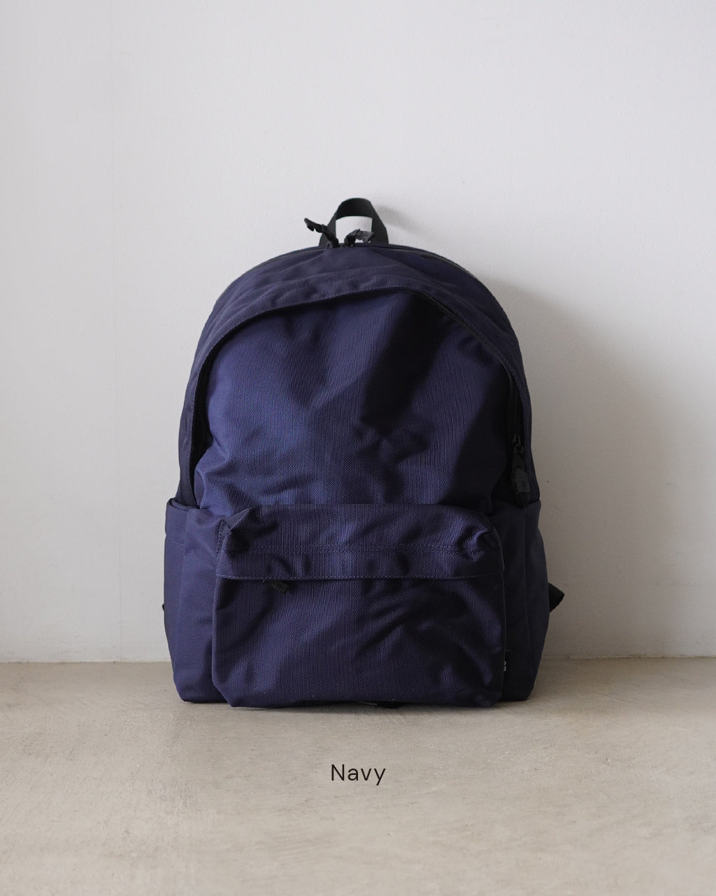 ネイビーの DAYPACK Mサイズ。前方の大きな収納ポケットとサイドポケット、背面にはパスポートポケットのないシンプルなリュック正面全体像