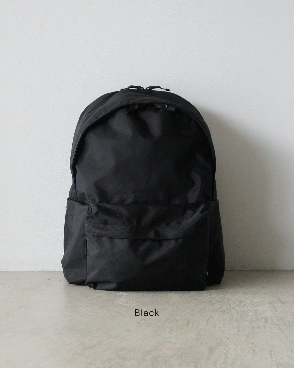 ブラックのDAYPACK Lsizeを正面から撮影したバックパック。シンプルなフォルムと前方の大容量ポケットが特徴的。