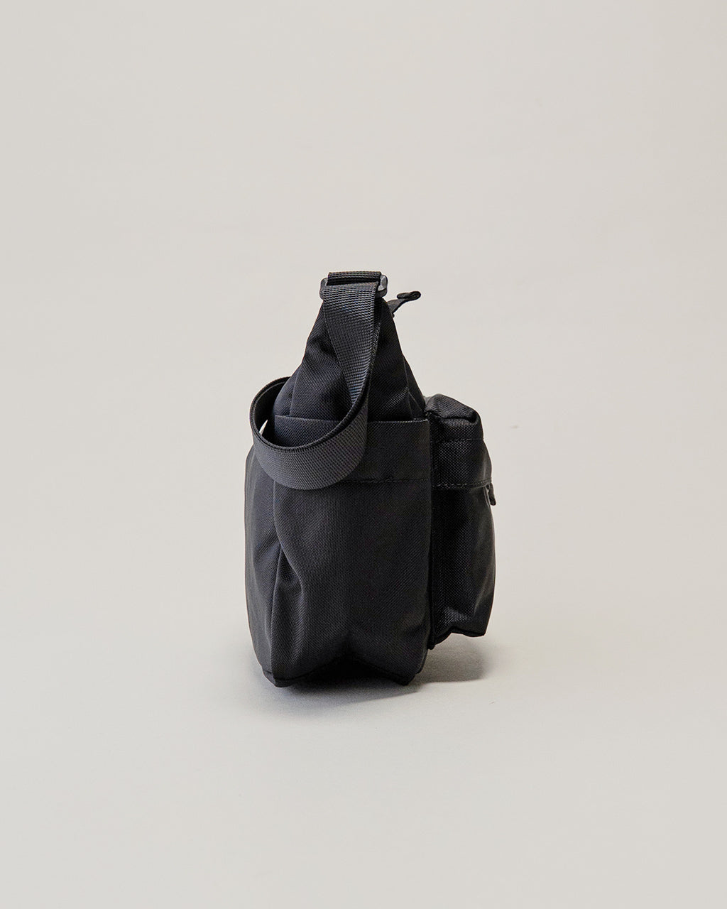 LC by LOWERCASEのショルダーバッグ Sサイズの横からの様子。ダークネイビー系の本体に、シンプルで実用的なハンドストラップとジップポケットが見える側面のディテールを捉えた写真。